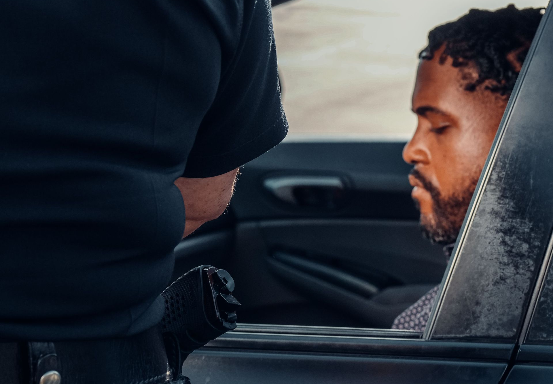 View our Service Area Police officer stands beside a man seated in a car, seen through the open window.