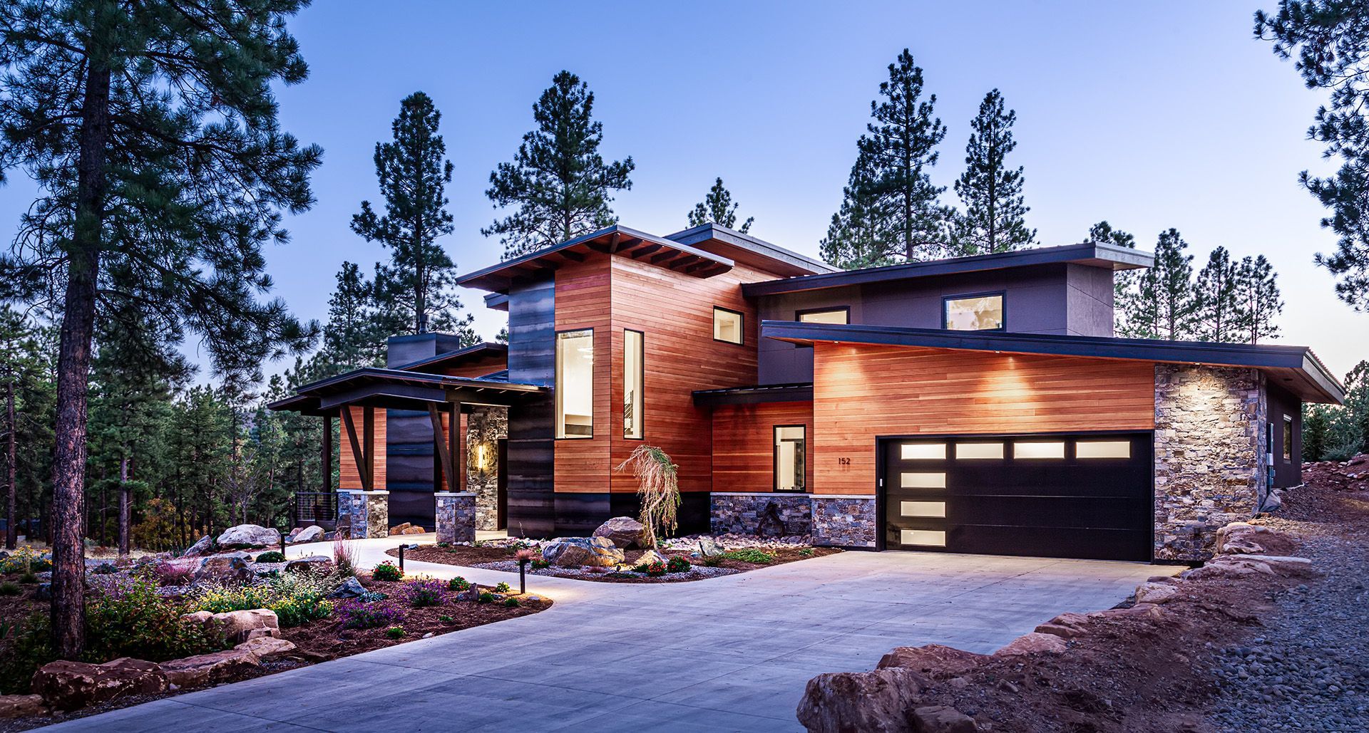 A large house with a black garage door is surrounded by trees.