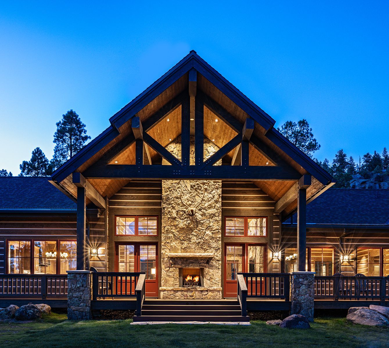 A large house in the middle of a forest with mountains in the background at sunset.