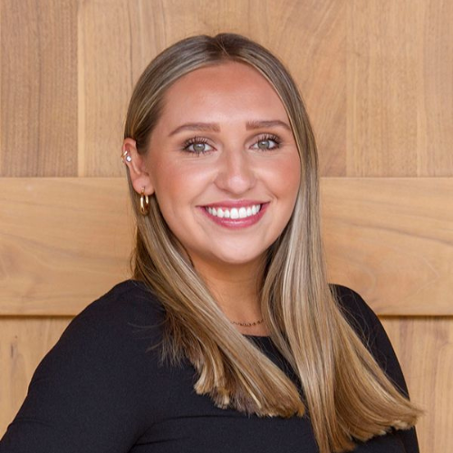 A woman in a black shirt is smiling in front of a wooden wall.