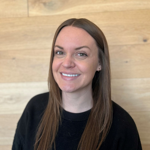 A woman in a black shirt is smiling while sitting on a couch.