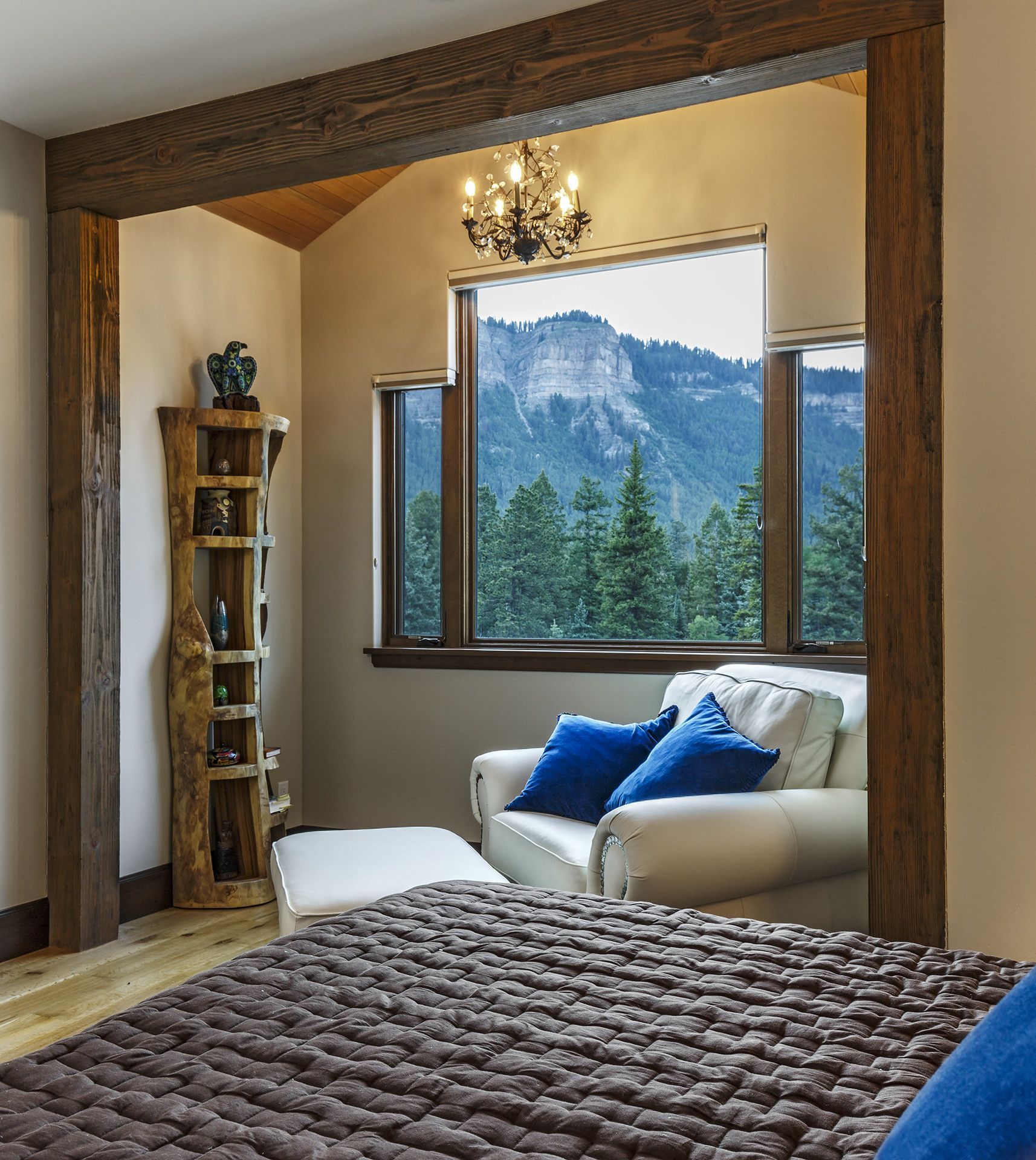 A bedroom with a bed a chair and a window with mountains in the background