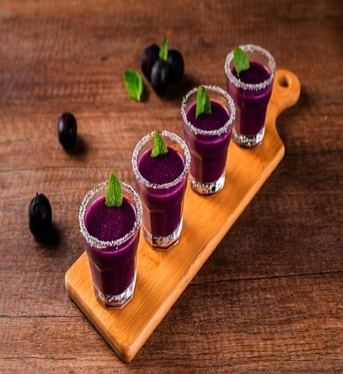 four shot glasses of purple liquid on a wooden cutting board