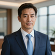 Professional headshot of a person in a navy suit and light blue tie, standing in a brightly lit office setting.