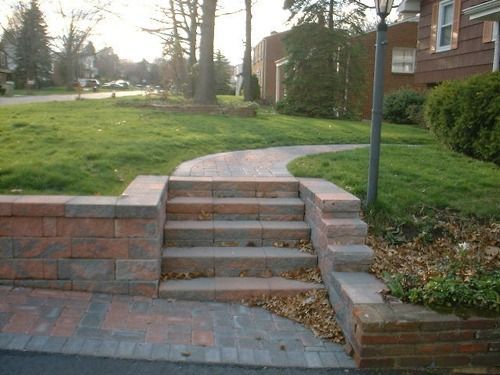 Brick steps leading to a curved path on a grassy lawn. Red brick retaining walls on either side.
