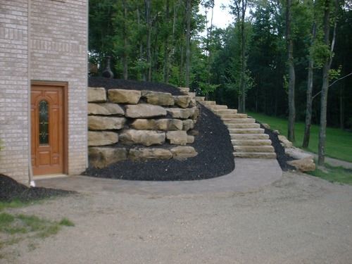 Exterior view with a stone retaining wall, stairs, and a house with a wooden door.