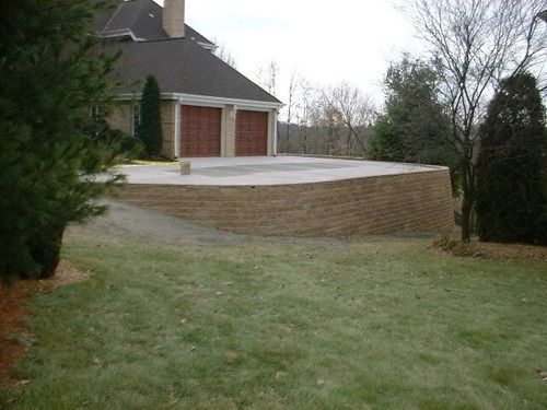 A raised concrete patio with a retaining wall next to a house with a garage.
