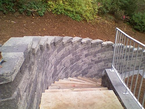 Stone steps descend into a curved, retaining wall, with a metal railing on the right.