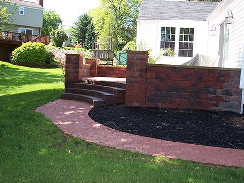 Brick patio with steps, brick pathway, and black mulch in a backyard setting.