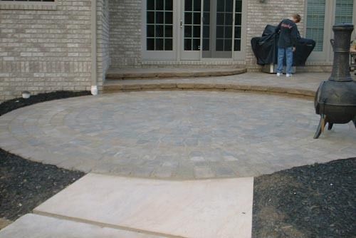 Circular paved patio with brick wall and double doors; person standing nearby.