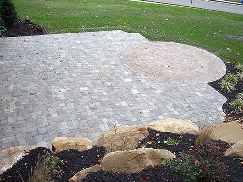 Patio with stone pavers and a circular design, surrounded by grass and landscaping.
