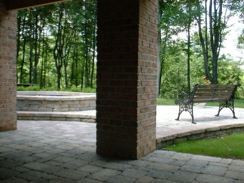 Brick patio with brick columns, stone fire pit, and bench, surrounded by trees.