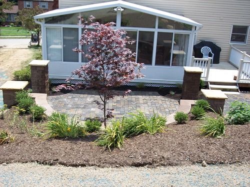 Small patio with tree and surrounding landscaping next to a white sunroom.