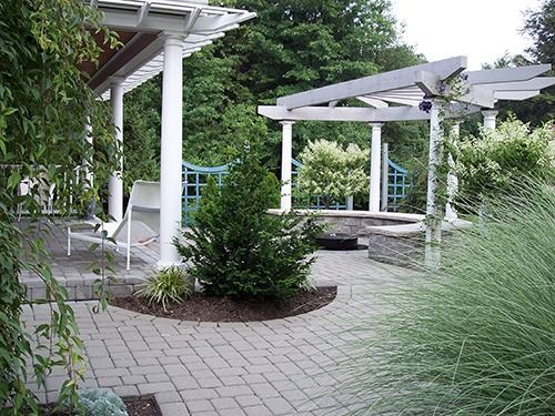 Patio with white pergolas, brick pavers, greenery, and blue accent fence.