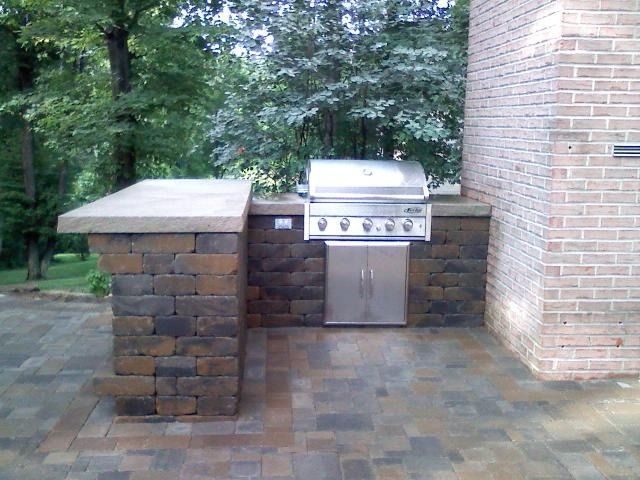 Outdoor brick grill station with countertop and stainless steel grill, on a patio.