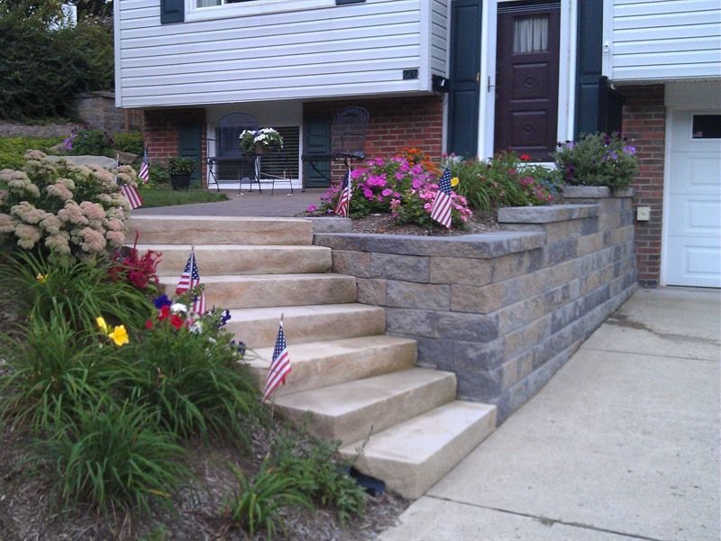 Stone steps and retaining wall leading to a house with American flags in garden beds.