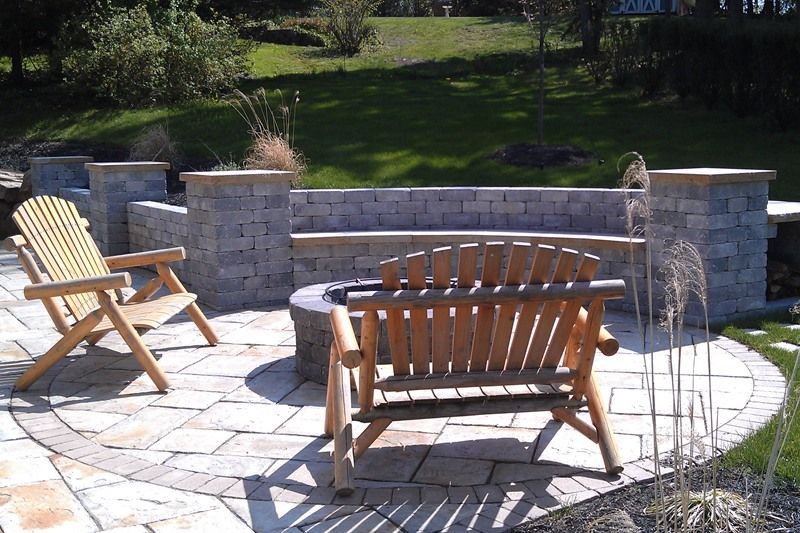 Patio with Adirondack chairs, stone bench, and fire pit; surrounded by landscaping.