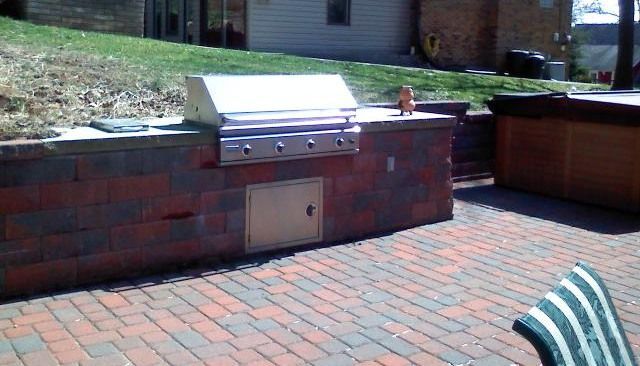Brick outdoor kitchen with a grill, red brick patio, and hot tub.