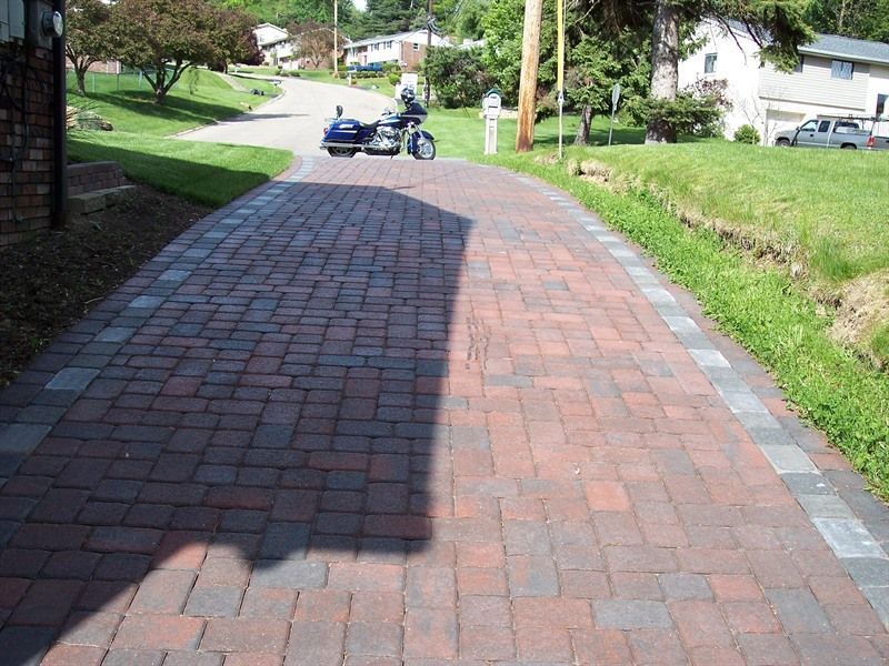 Brick driveway with a motorcycle parked on it, surrounded by green grass and a suburban neighborhood.