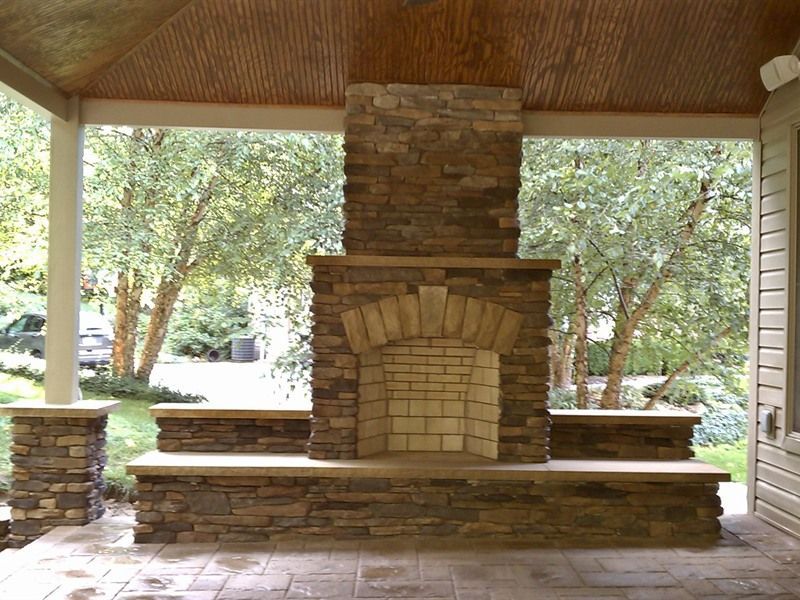 Stone fireplace with brick hearth on an outdoor patio under a wooden ceiling.