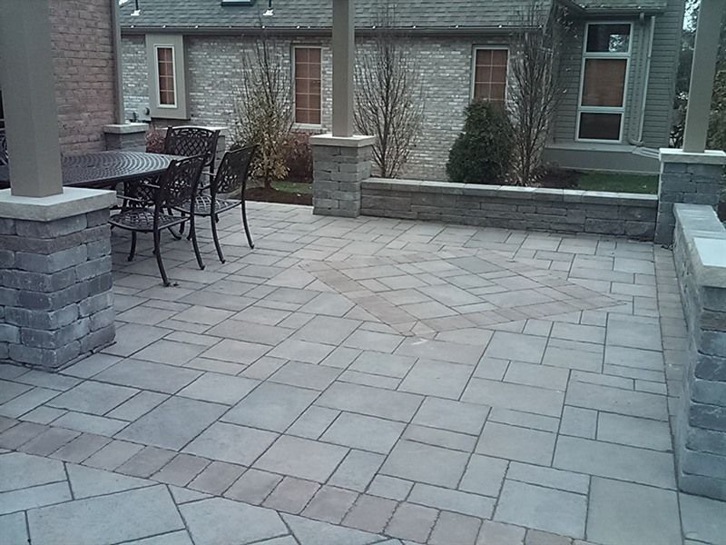 Stone patio with a dining set under a covered area, surrounded by low stone walls.