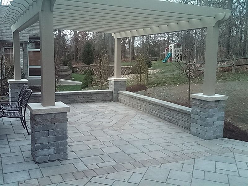 Pergola with brick columns and gray patio. Backyard setting, with a play structure visible.