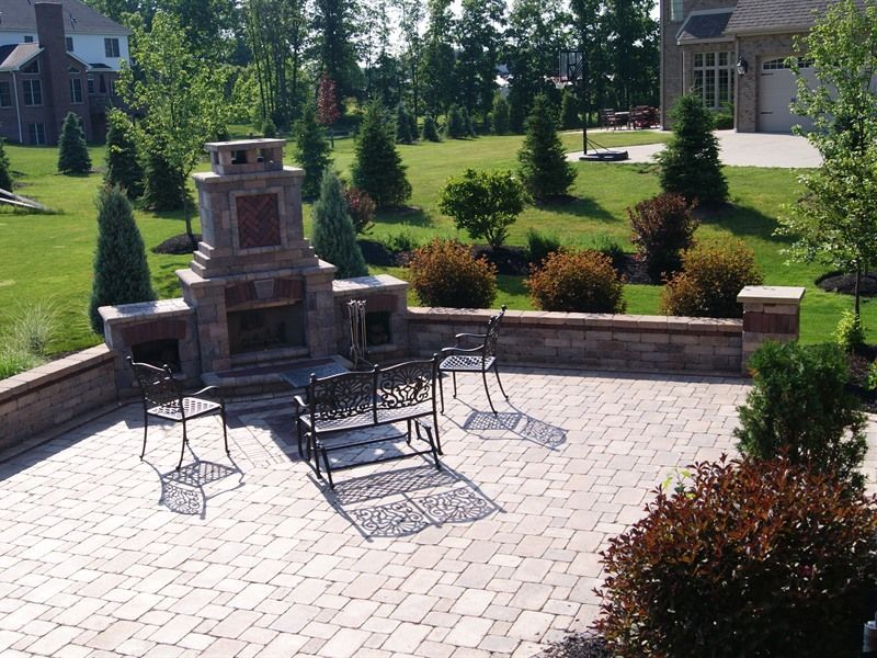 Brick patio with outdoor fireplace and seating, surrounded by landscaping and lawn.