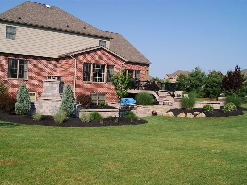 Backyard with brick house, landscaping, and a grassy lawn on a sunny day.
