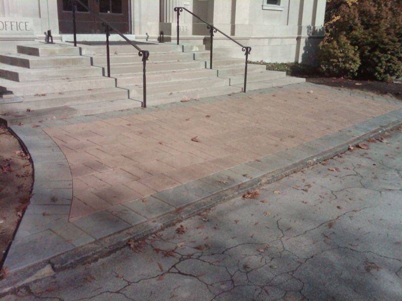 Brick ramp and steps leading to a building with a dark door. Black railings and concrete borders.