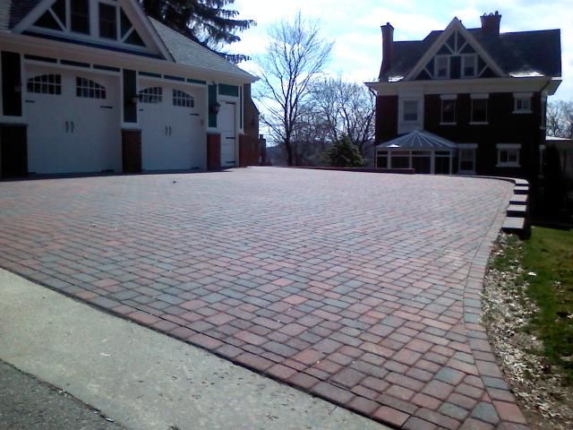 Brick driveway in front of a house with a garage and a house with a sunroom.