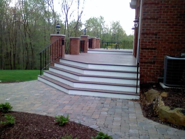 Brick home with a multi-level deck featuring stairs, brick pillars, and a black railing.