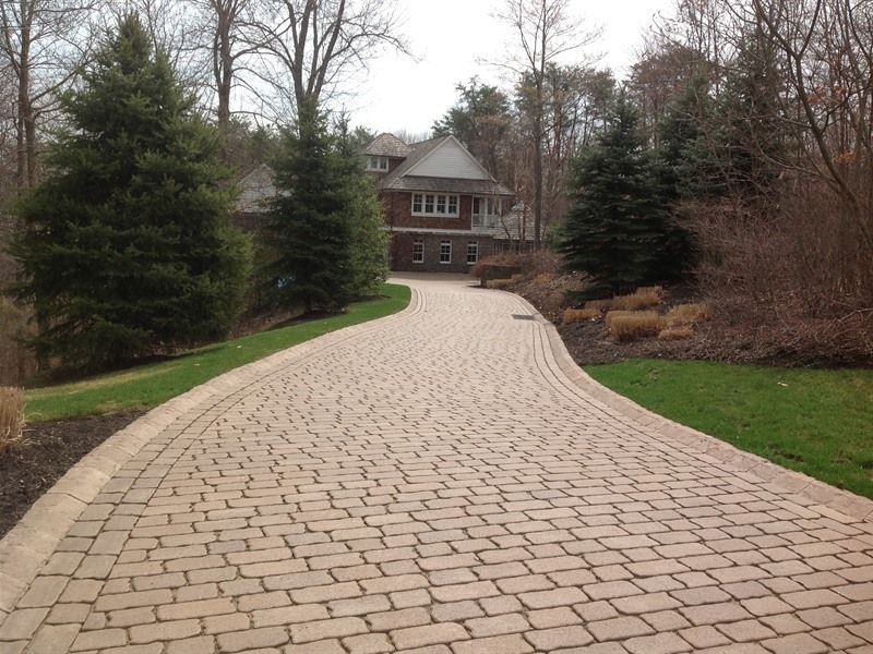 Brick driveway leading to a house with trees on either side.