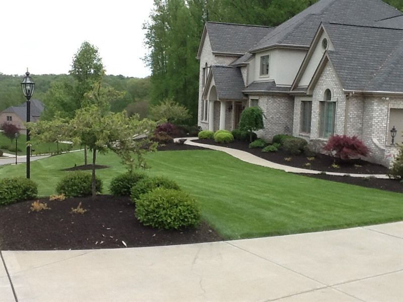 Well-manicured house with a curved walkway and lush landscaping. Green lawn, trees, and dark mulch beds.
