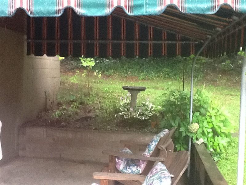 A wooden porch swing under a striped awning overlooks a garden with a bird bath.