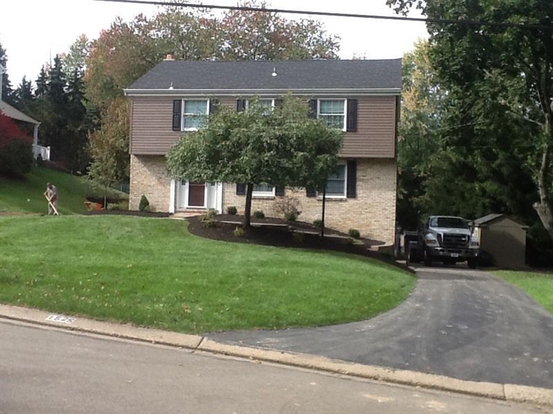 Two-story house with brick base and brown siding. Lush lawn, driveway, truck parked in front.