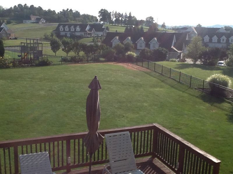 View from a deck of a large green lawn, black fence, and houses on a hill. Brown patio umbrella and chairs.