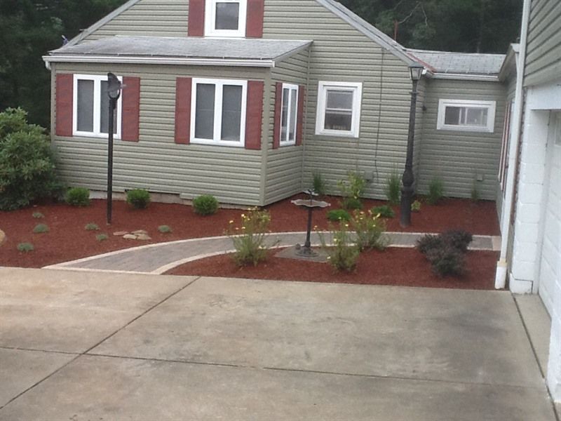 Green house with a red-mulched garden, paved path, and concrete driveway.