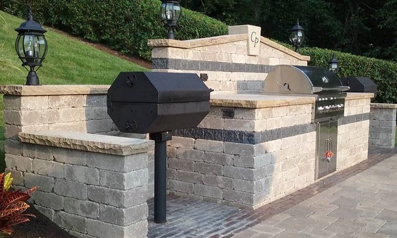 Outdoor kitchen with stone walls and a built-in grill, smoker, and countertops.