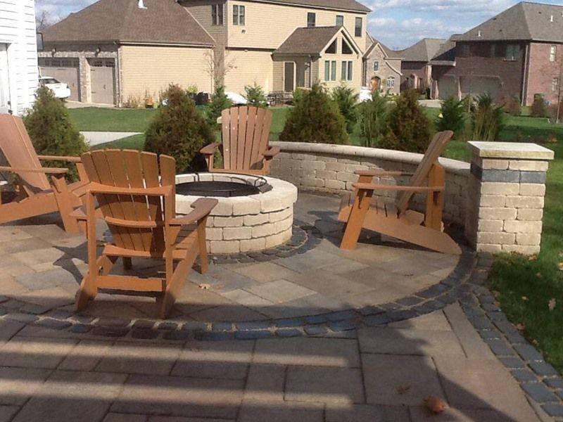 Patio with a fire pit, Adirondack chairs, and low stone wall in a suburban setting.
