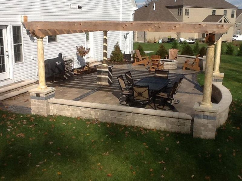 Patio with dining table, chairs, and pergola with wooden beams, near house and grass.