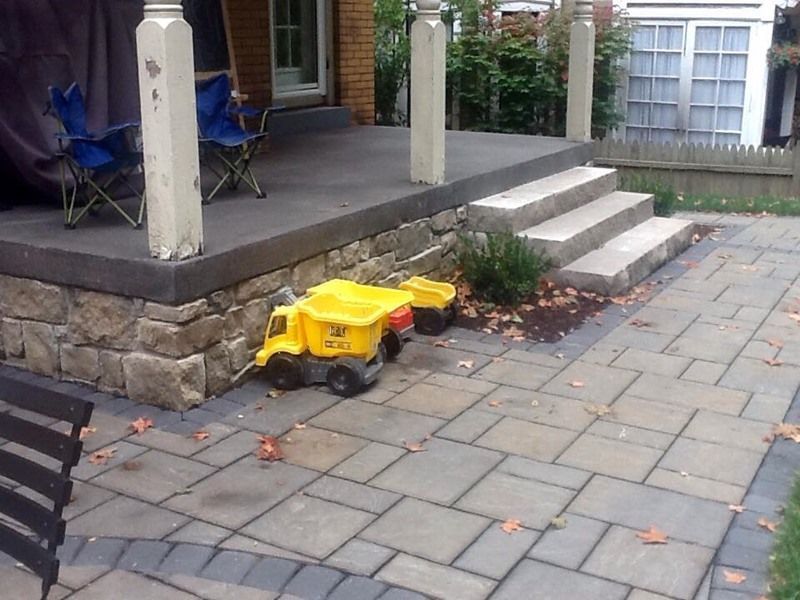 Yellow toy trucks on a stone patio near a porch with stone steps.