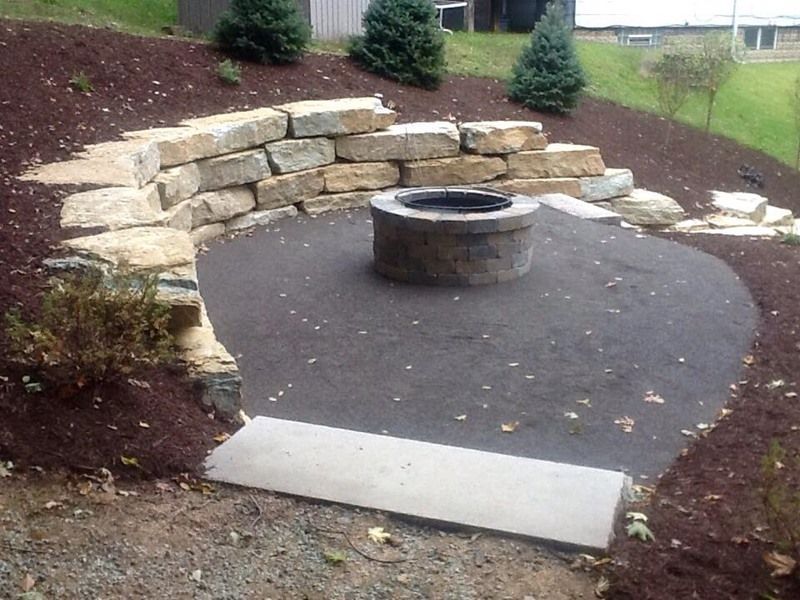 Stone fire pit area with retaining wall on a hillside, dark ground cover.