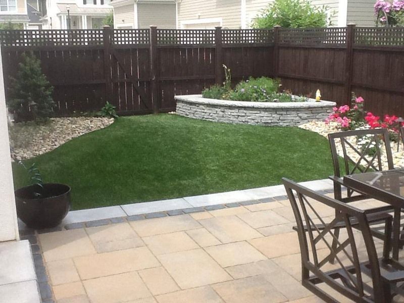 Patio with outdoor furniture, stone patio, green lawn, flower bed, and brown wooden fence.