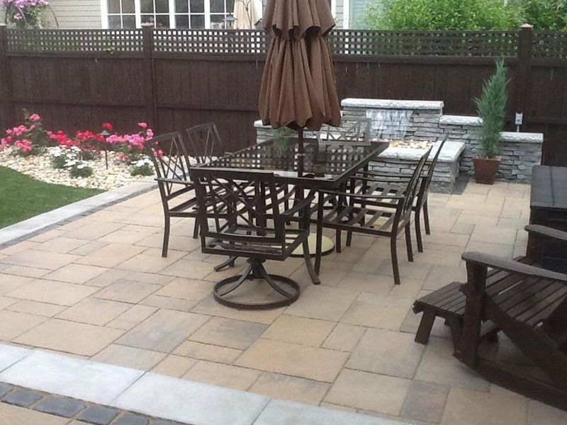 Patio with dining set, umbrella, and stone wall with a small waterfall.