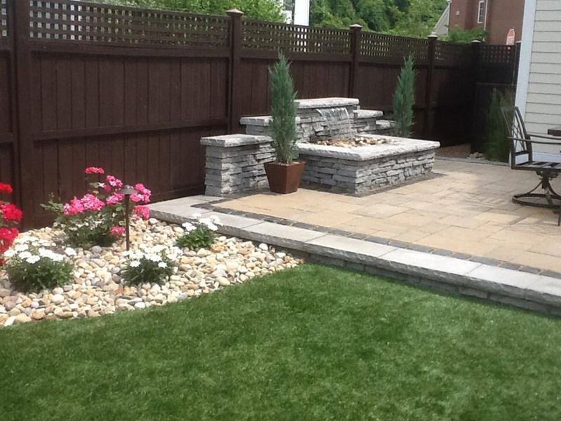 Backyard patio with stone water feature, brown fence, and flower bed.