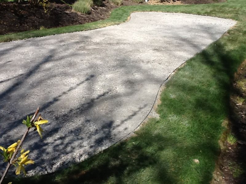 Gravel patio surrounded by grass and flower beds. Sunlight casts shadows on the patio.