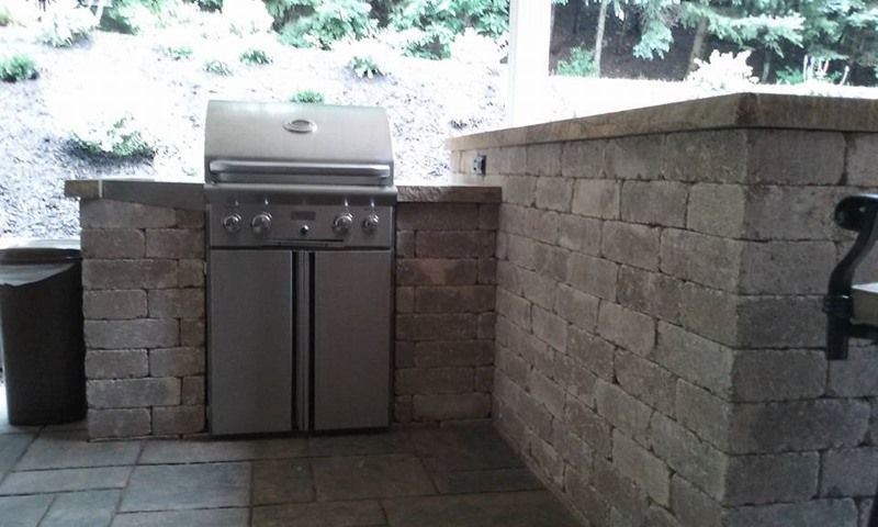 Outdoor kitchen with stainless steel grill built into a stone structure.