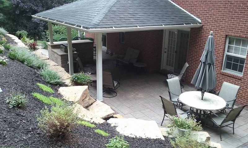 Patio with seating under a canopy, alongside a landscaped garden on a hillside.