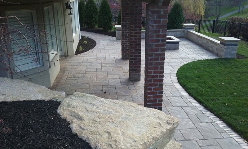 Stone patio with brick columns and a large rock in a landscaped yard.