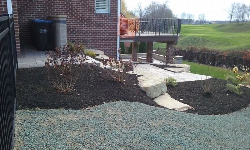 Landscaped backyard with mulch, stone path, deck, brick house, and green lawn.